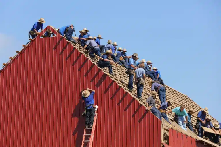 A group of handwerkers working on the roof of a red barn.